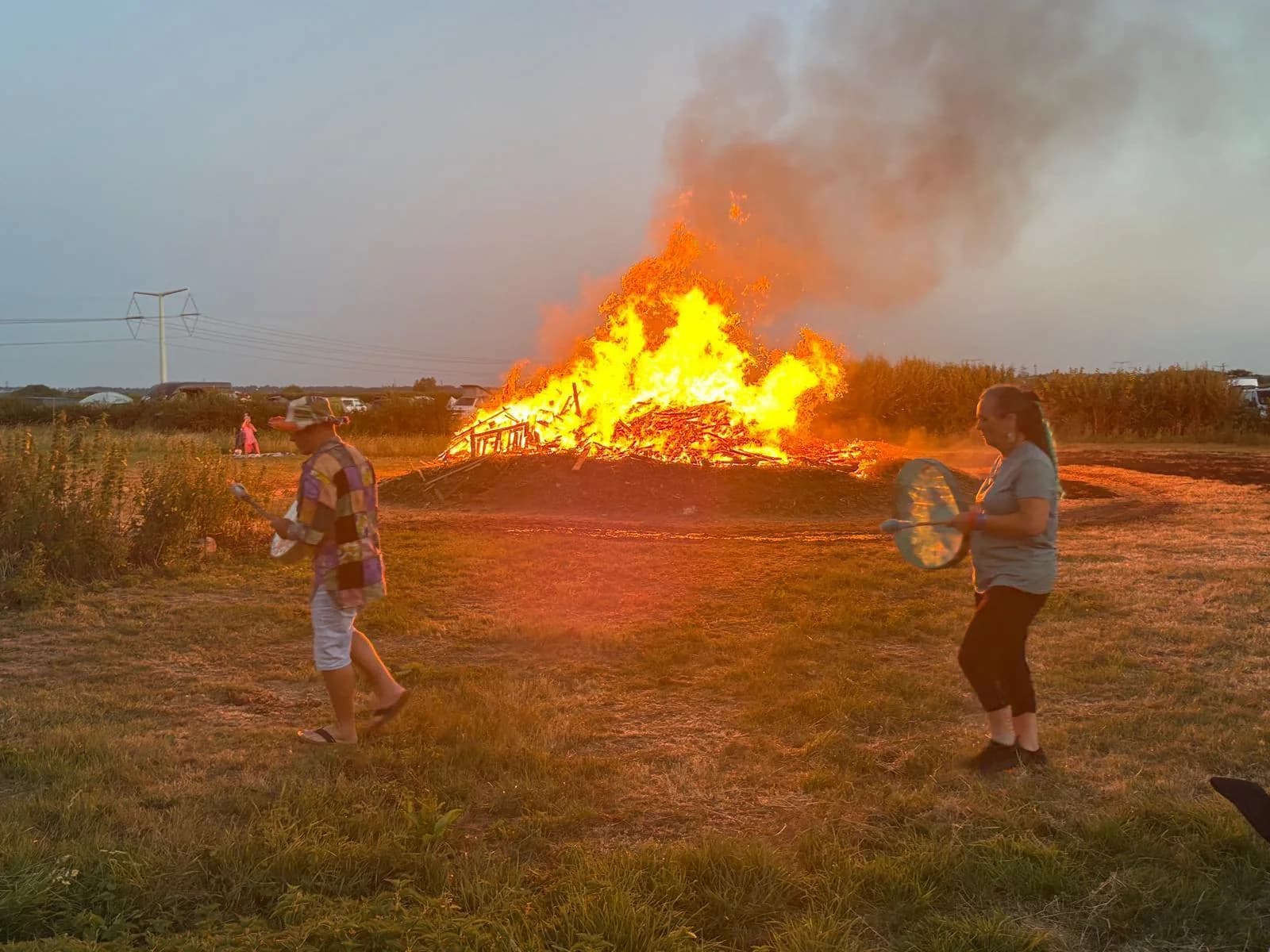Campers walking with hand drums beside the campfire at sunset